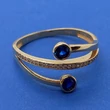 Középen sorkővel kirakott, két oldalt buttonos foglalatba foglalt kék színű cirkon kővel díszített arany gyűrű