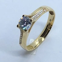 Középen 4 karomba foglalt kerek gyémánt csiszolású, két oldalt ellentétes irányba, fehér cirkon kövekkel díszített arany eljegyzési gyűrű