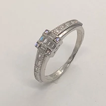 Fejrészen kiszélesített négyzet alakú kő berakásos foglalatú, két oldalán szintén négyzet hatásul kövekkel díszített ezüst gyűrű